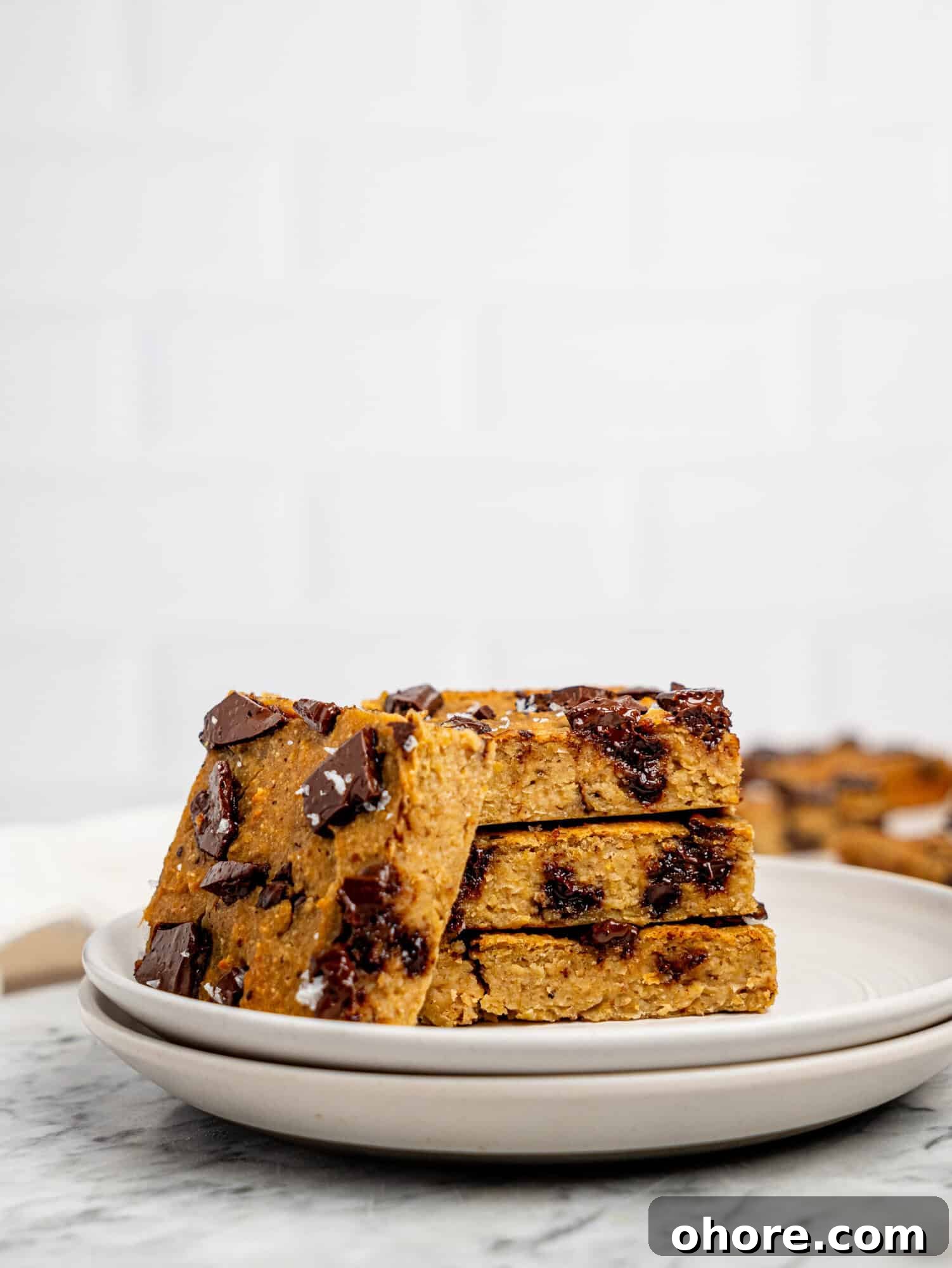 Gooey Chickpea Cookie Bars — Protein-Packed Dessert Bars 2 Healthy cookie bars with dark chocolate stacked on a white plate.