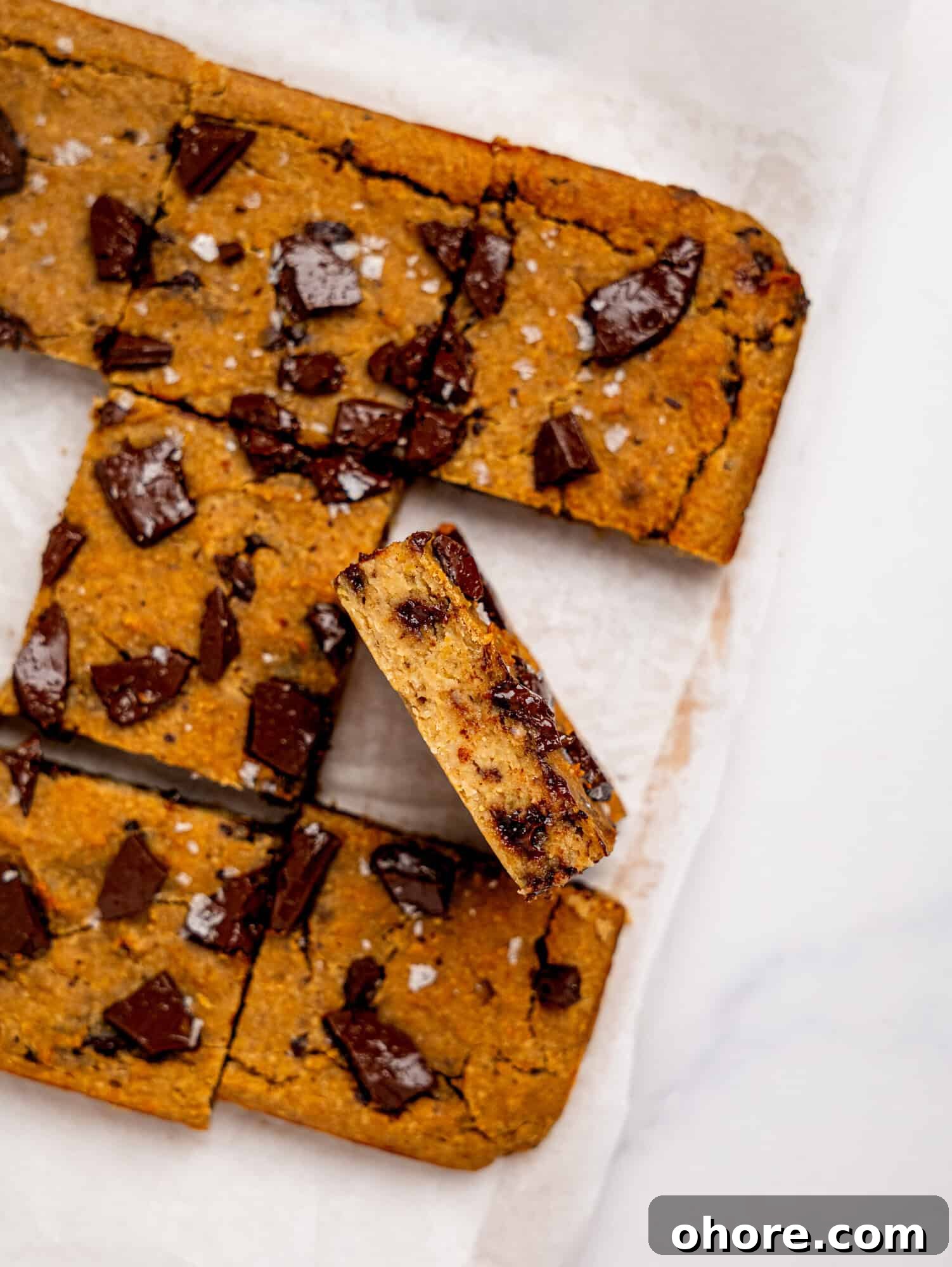 Gooey Chickpea Cookie Bars — Protein-Packed Dessert Bars 6 Bird's eye view of chickpea cookie bars on a sheet of white parchment paper, one is turned on its side to reveal the fudgy texture.