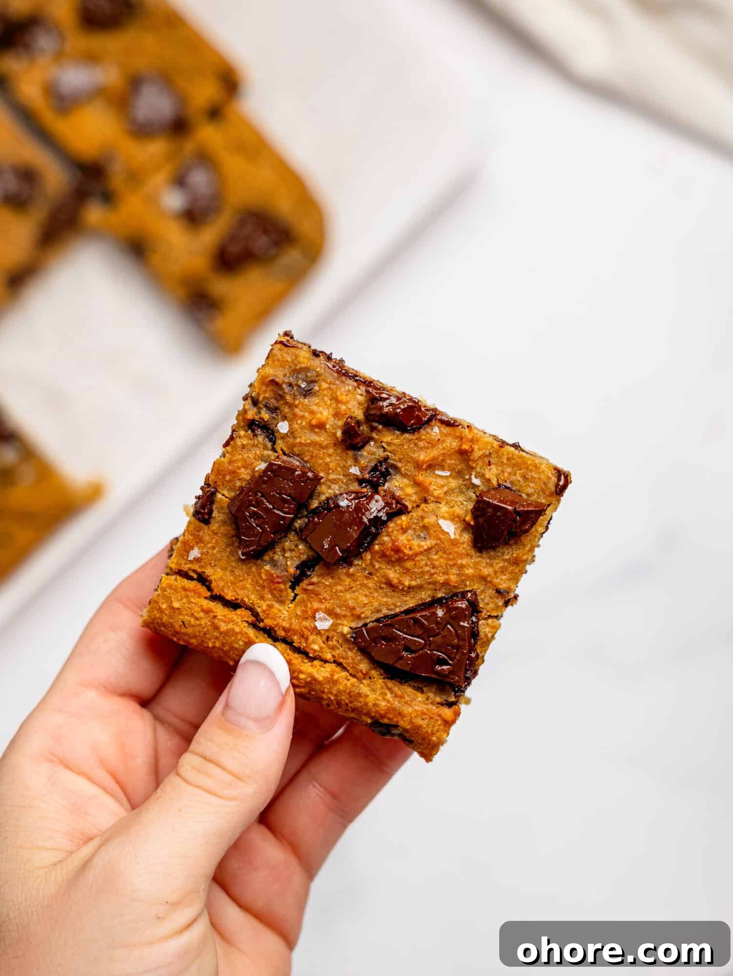 Gooey Chickpea Cookie Bars — Protein-Packed Dessert Bars 7 A hand holding a chickpea cookie bar with dark chocolate.