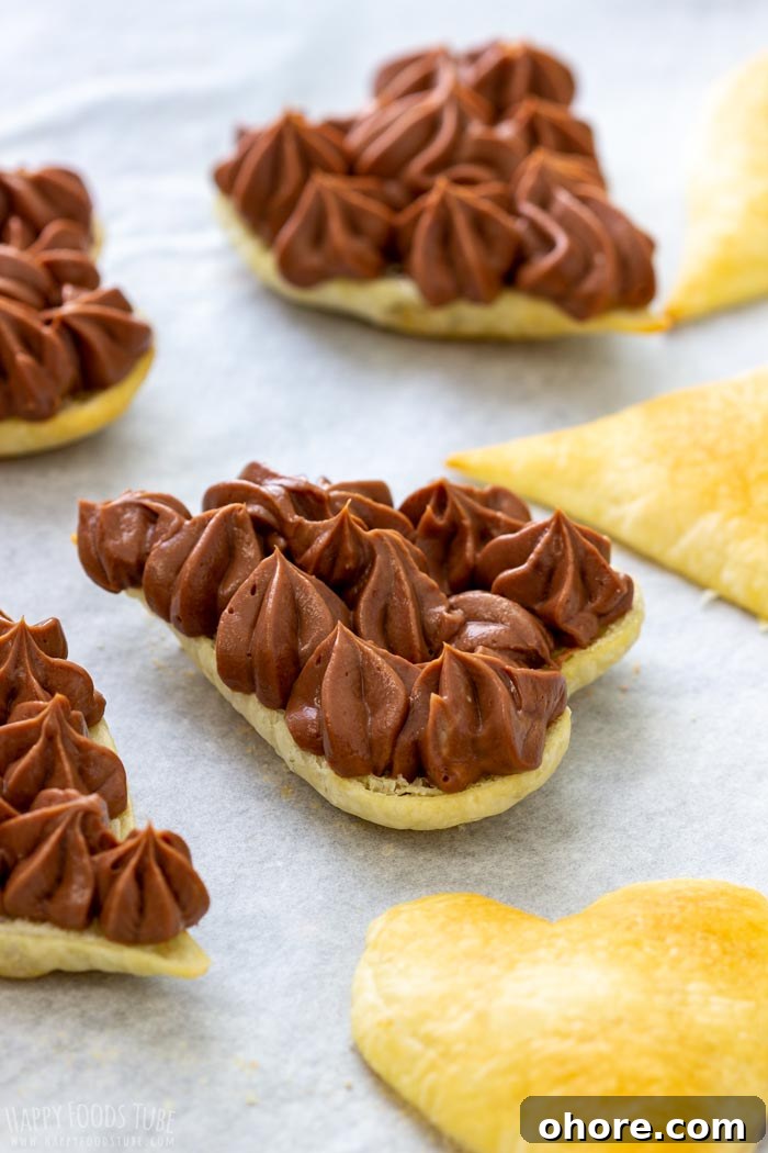 Flaky Puff Pastry Hearts for Valentine’s Day Gifts 5 Heart-shaped puff pastry topped with chocolate filling on parchment paper.