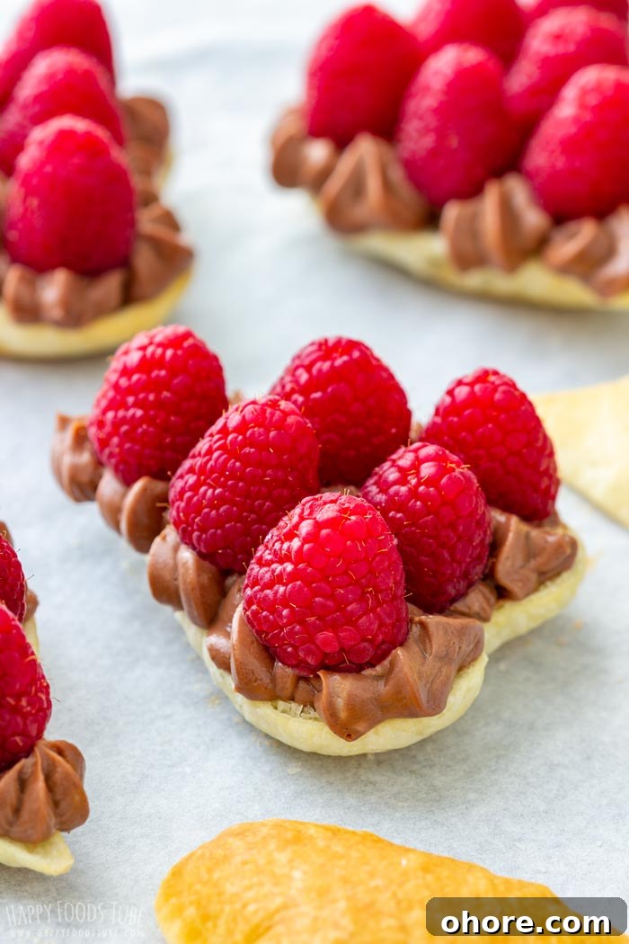 Flaky Puff Pastry Hearts for Valentine’s Day Gifts 6 Heart-shaped puff pastry topped with chocolate filling and raspberries on parchment paper.