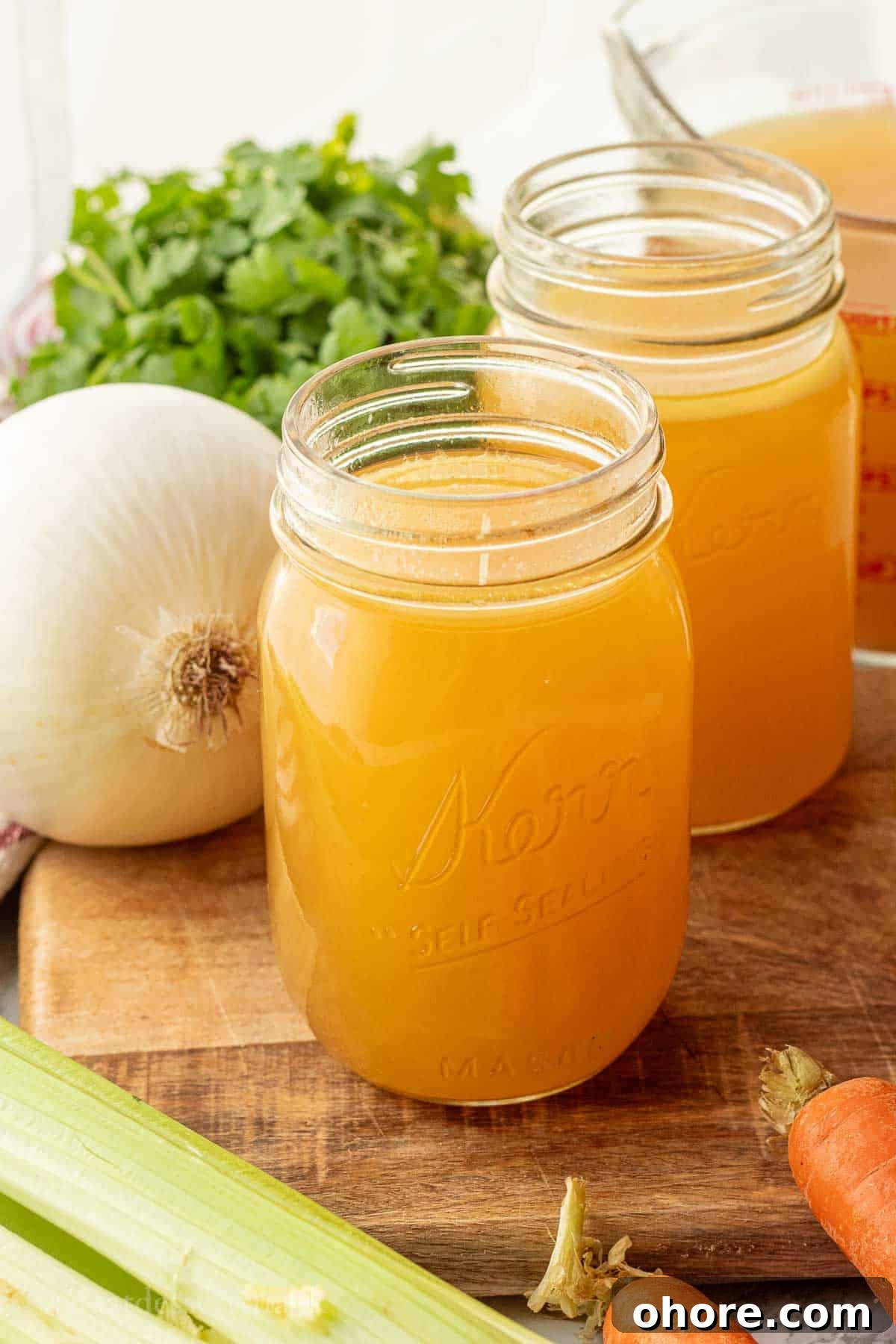 Homemade Instant Pot Chicken Bone Broth Recipe 2 Chicken bone broth in jar on wood cutting board with veggies.