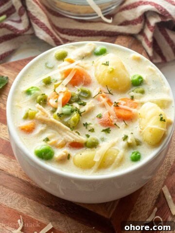 White bowl of chicken gnocchi soup on wood cutting board.
