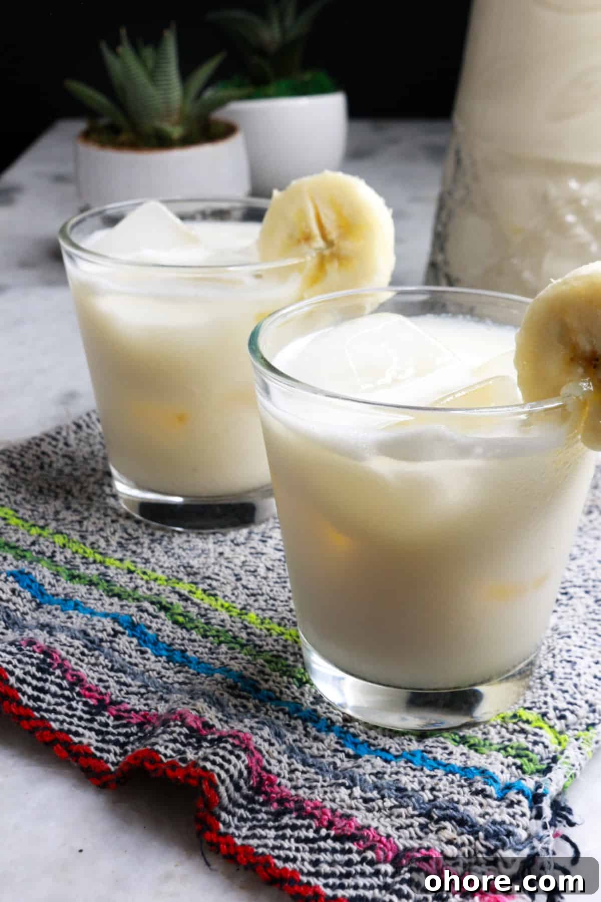 Banana Agua Fresca Recipe — Refreshing Banana Water Drink 2 Two glasses with ice and agua de platano garnished with a slice of banana