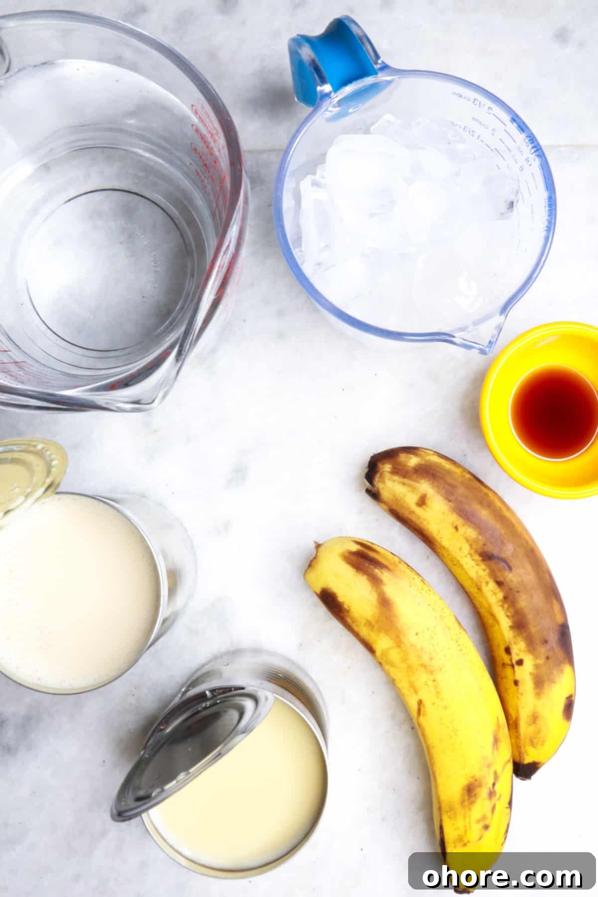Banana Agua Fresca Recipe — Refreshing Banana Water Drink 3 Measuring cup with water, another with ice, a can of evaporated milk, a can of condensed milk, 2 bananas, a small bowl with vanilla extract