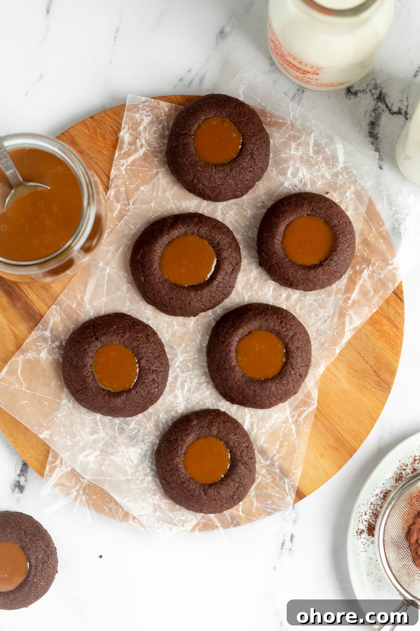 Chewy Dulce de Leche Sandwich Cookies 4 A wooden tray topped with chocolate thumbprint cookies and a jar of dulce de leche.