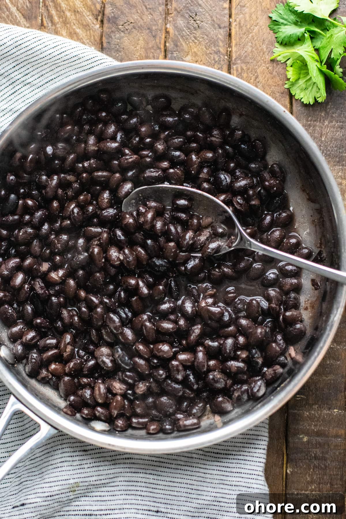 Quick Black Bean Tacos Ready in 10 Minutes 4 black beans cooking in stainless steel pan with spoon mixing.