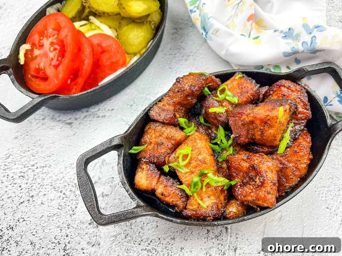 A plate of smoked pork belly burnt ends with tomatoes and pickles.