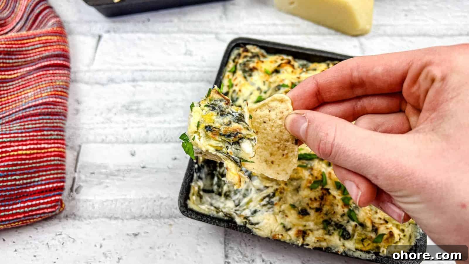 A hand dipping a tortilla chip into a tray of Copycat Applebee’s spinach artichoke dip.