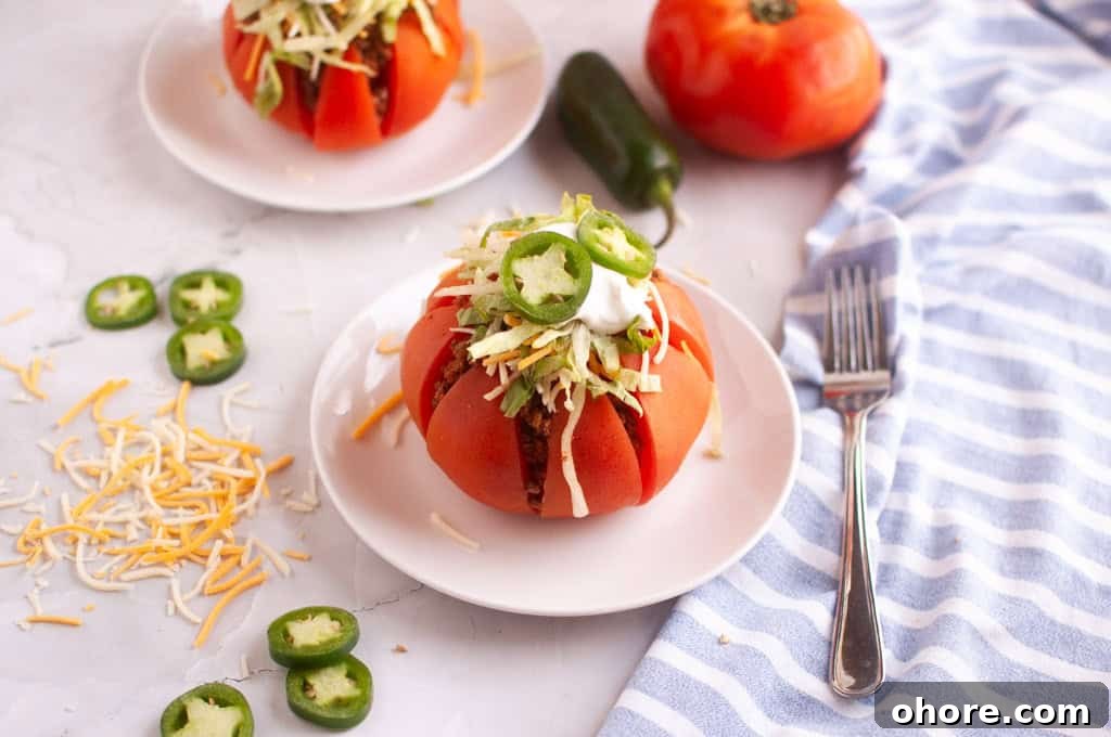 Two taco stuffed tomatoes on white plates with toppings and a fork.