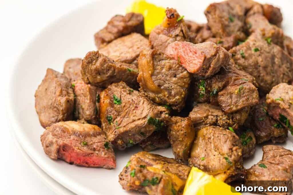 A plate of cooked steak bites garnished with herbs, served with pieces of yellow bell pepper.