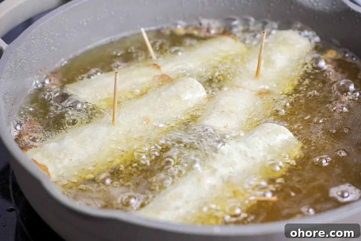 Crispy Chicken Flautas Recipe: Authentic Mexican Street-Style Tortillas 4 Rolled flautas recipe frying in a pan of oil.