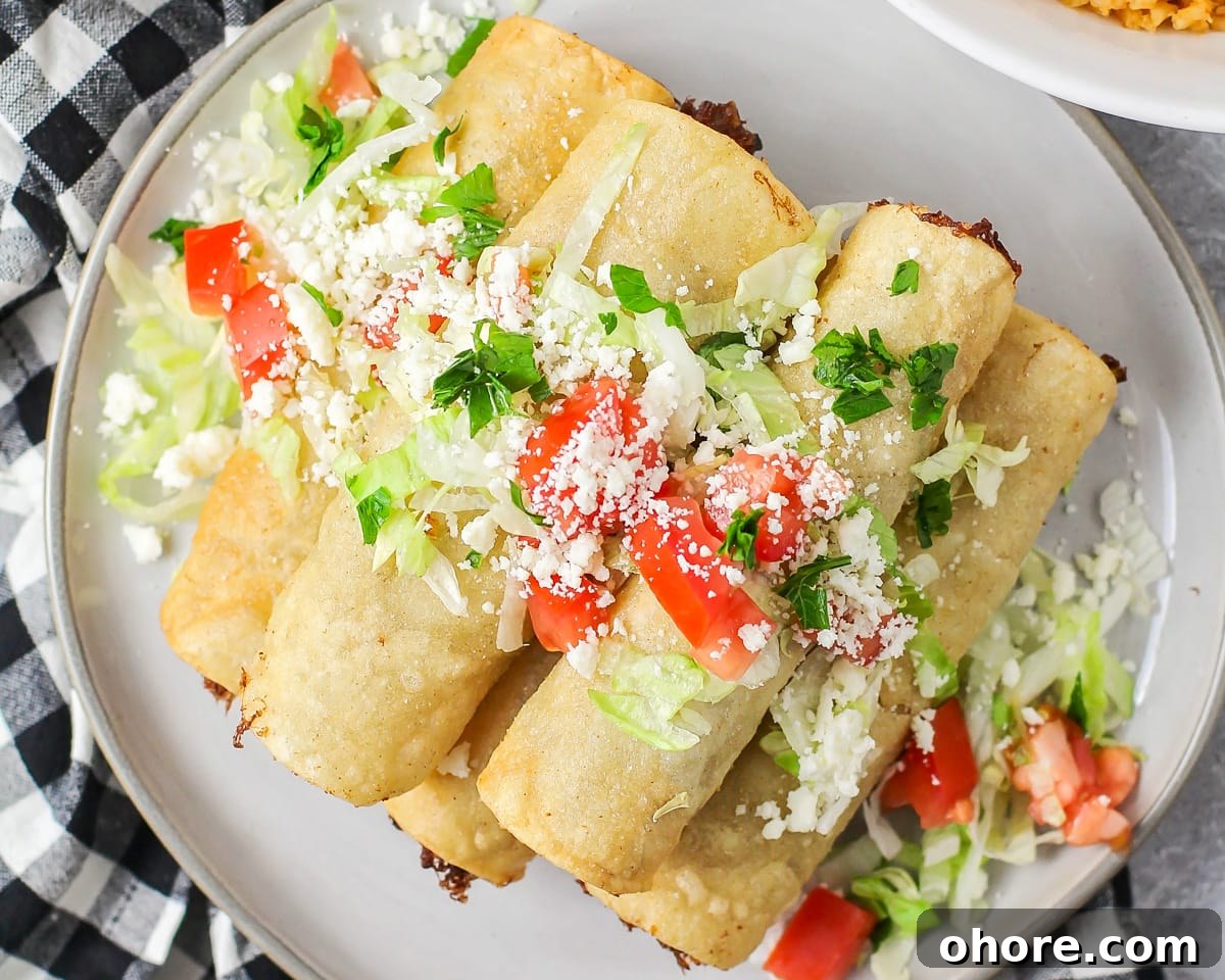 Crispy Chicken Flautas Recipe: Authentic Mexican Street-Style Tortillas 6 A pile of beef flautas topped with cotija, tomatoes, and cilantro.