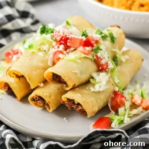 Crispy Chicken Flautas Recipe: Authentic Mexican Street-Style Tortillas 7 Flautas recipe stacked on each other with lettuce, cheese and chopped tomatoes on top.
