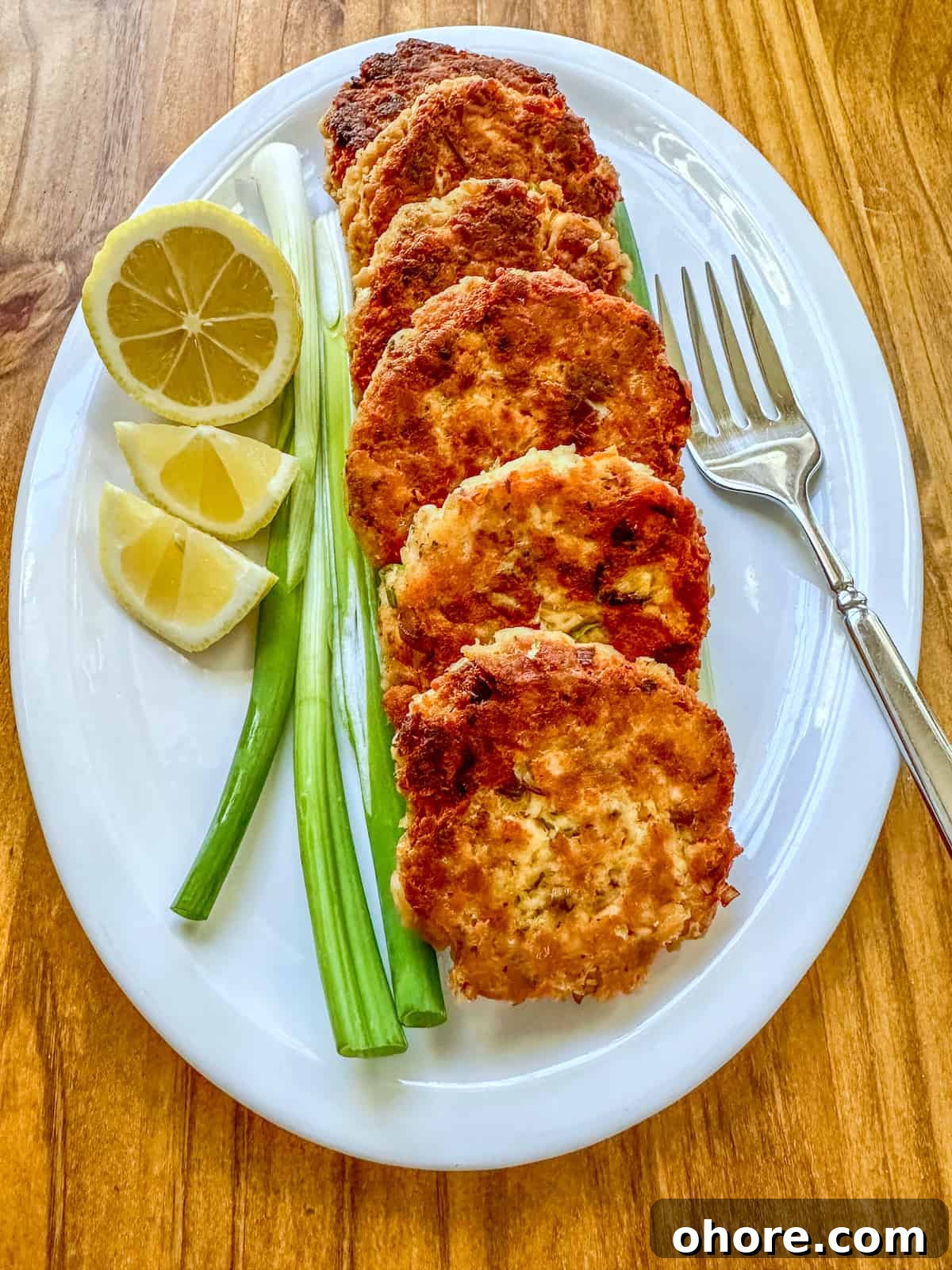 Cooked salmon patties on a plate with scallions, lemons and a fork.
