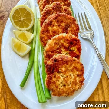 Cooked salmon patties on a plate with scallions, lemons and a fork.