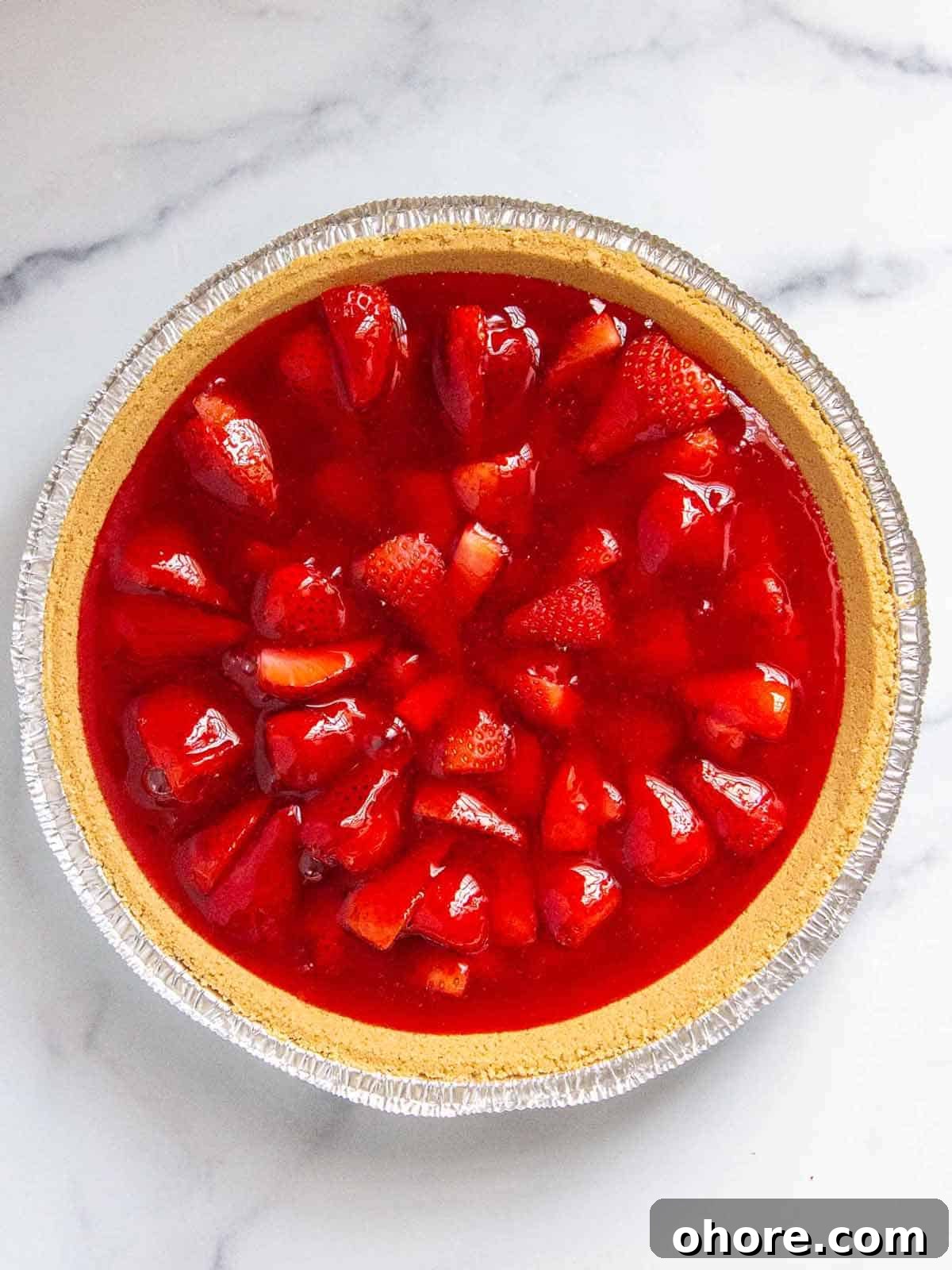 Strawberries cut side facing down in a graham cracker pie crust with jello poured evenly over top.
