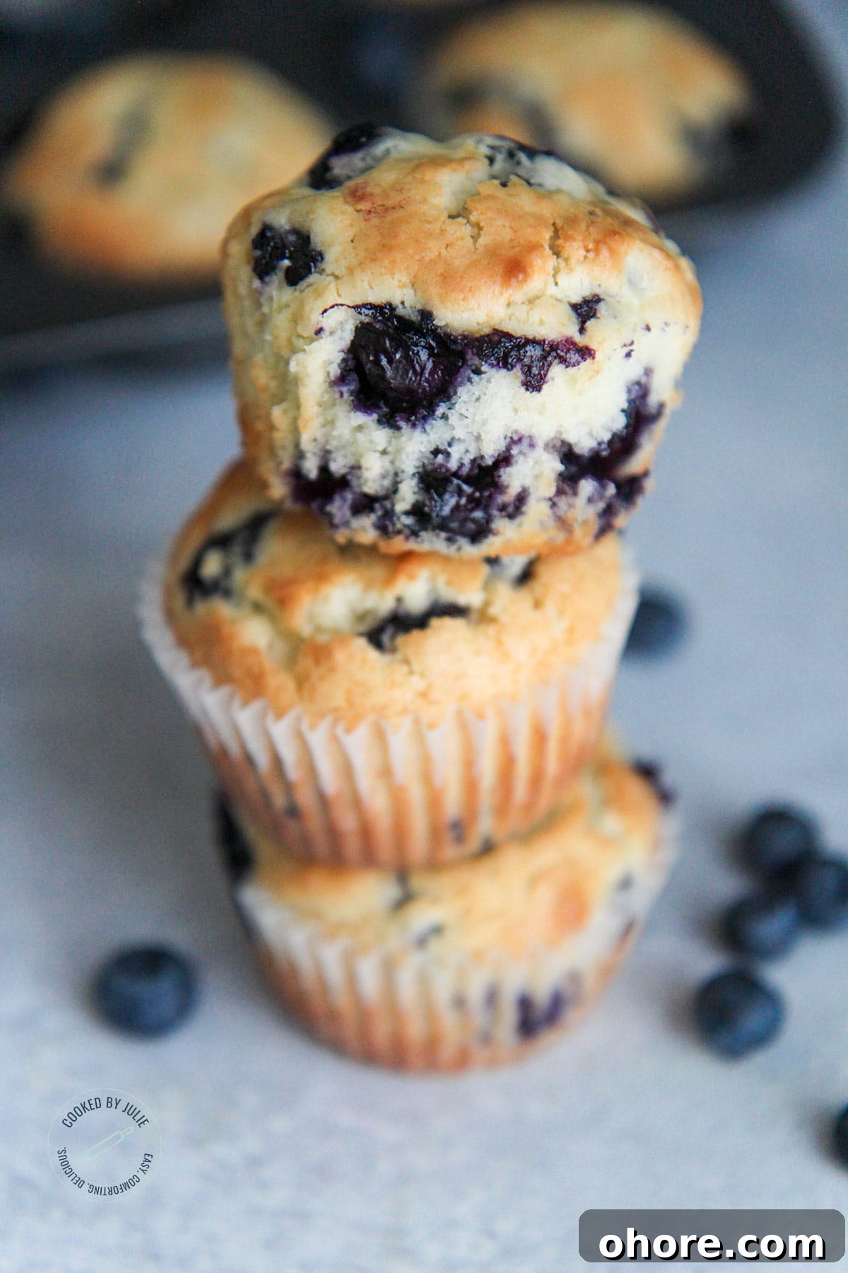 three blueberry muffins stacked with fresh blueberries on the side