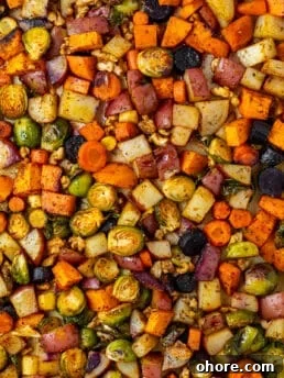 sweet potatoes, carrots, potatoes and brussels sprouts on a sheet pan with walnuts and honey butter glaze