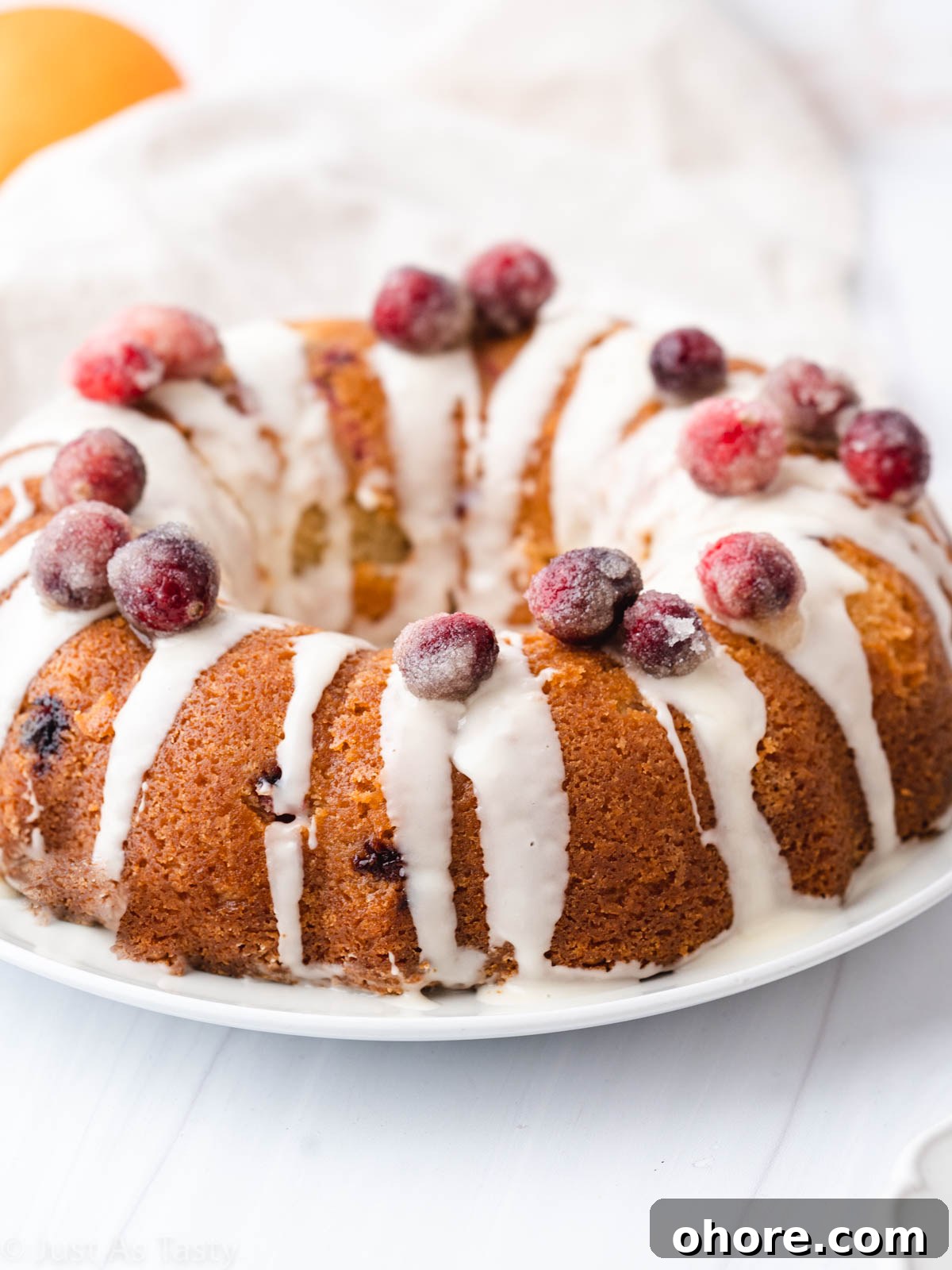 Cranberry Orange Bundt Cake with Zesty Citrus Glaze 7 Cranberry orange bundt cake topped with orange glaze and sugared cranberries on a white plate.