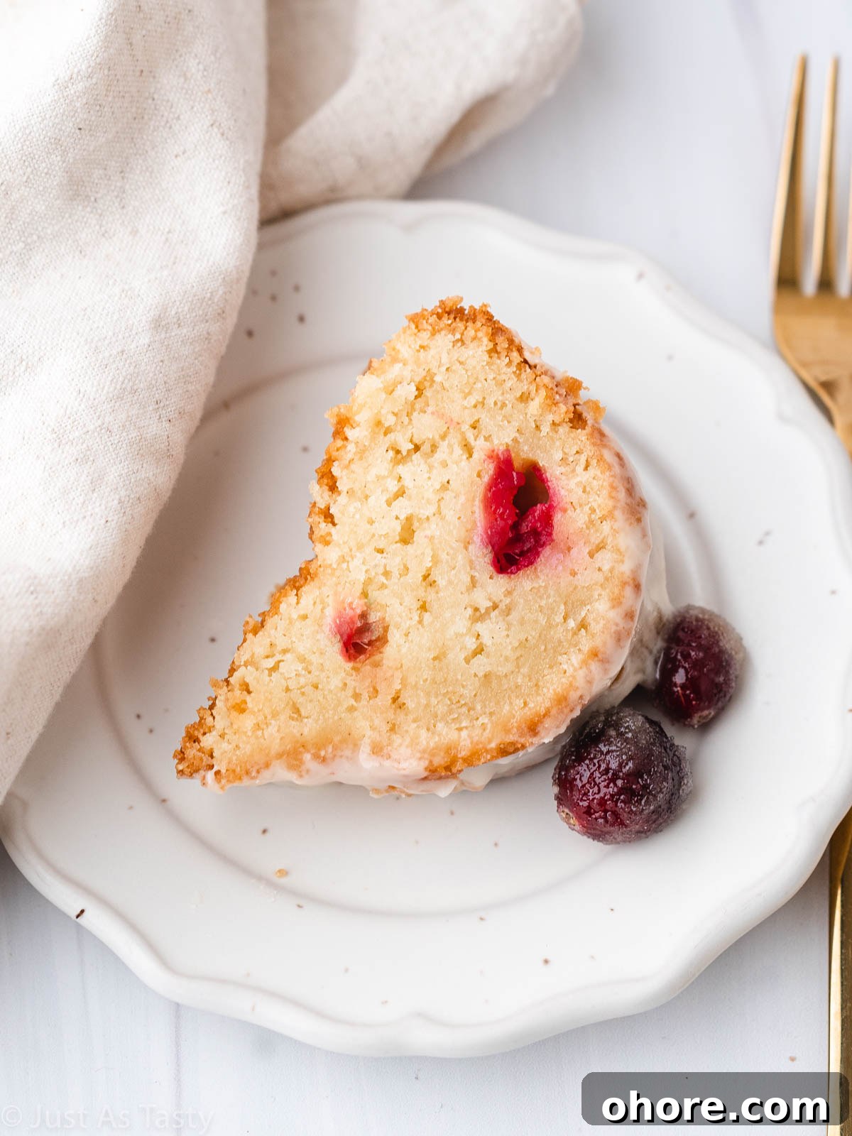 Cranberry Orange Bundt Cake with Zesty Citrus Glaze 8 A slice of glazed cranberry orange bundt cake on a white plate.