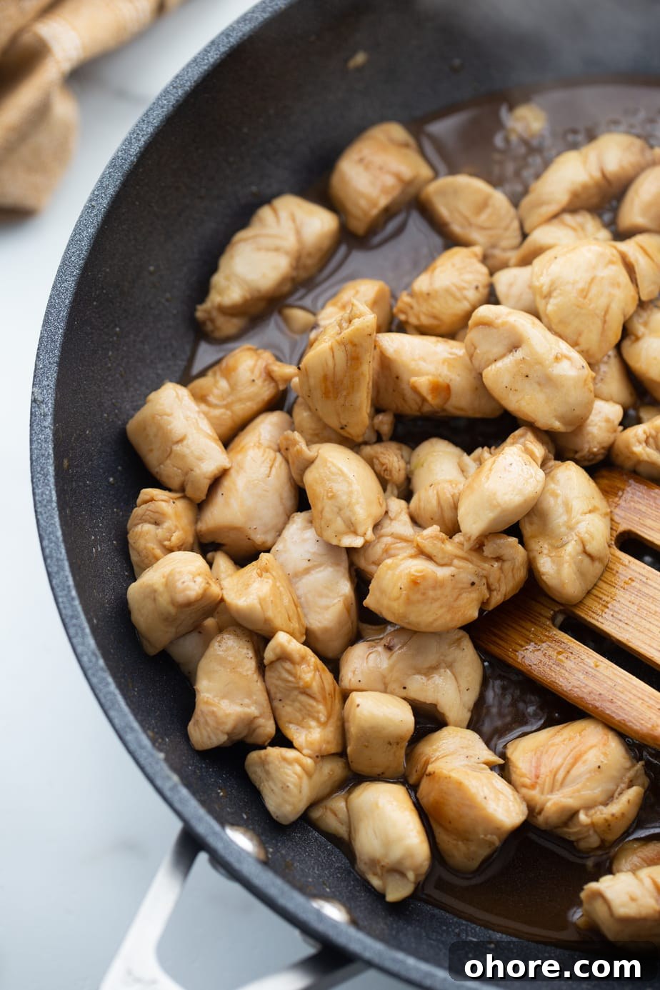 Hibachi Chicken Recipe: Tender Grilled Chicken with Garlic Butter 6 Browned chicken is being stirred by a wooden spoon in a black skillet.