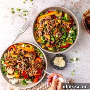 Two white bowls with ground beef stir fry in it and sauce to the side.