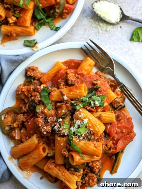 White plate with saucy noodles and pepperonis.