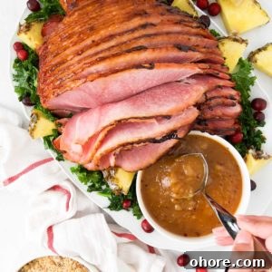 A person lifts a spoon of pineapple ham glaze sitting next to a roasted ham