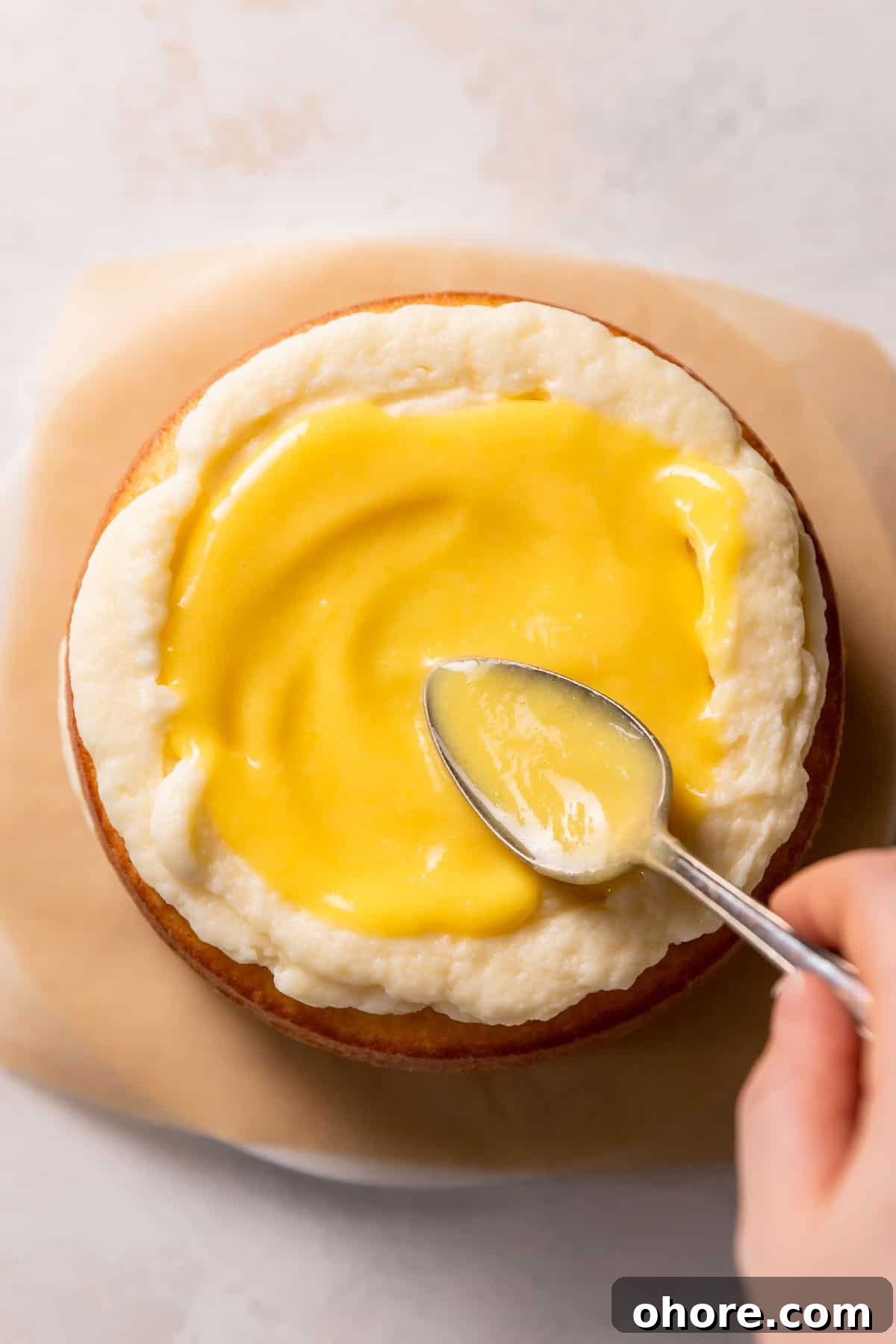 Zesty Lemon Bar Cake Recipe with Tender Shortbread Crust 12 a hand spooning lemon curd on top of the cake layer.