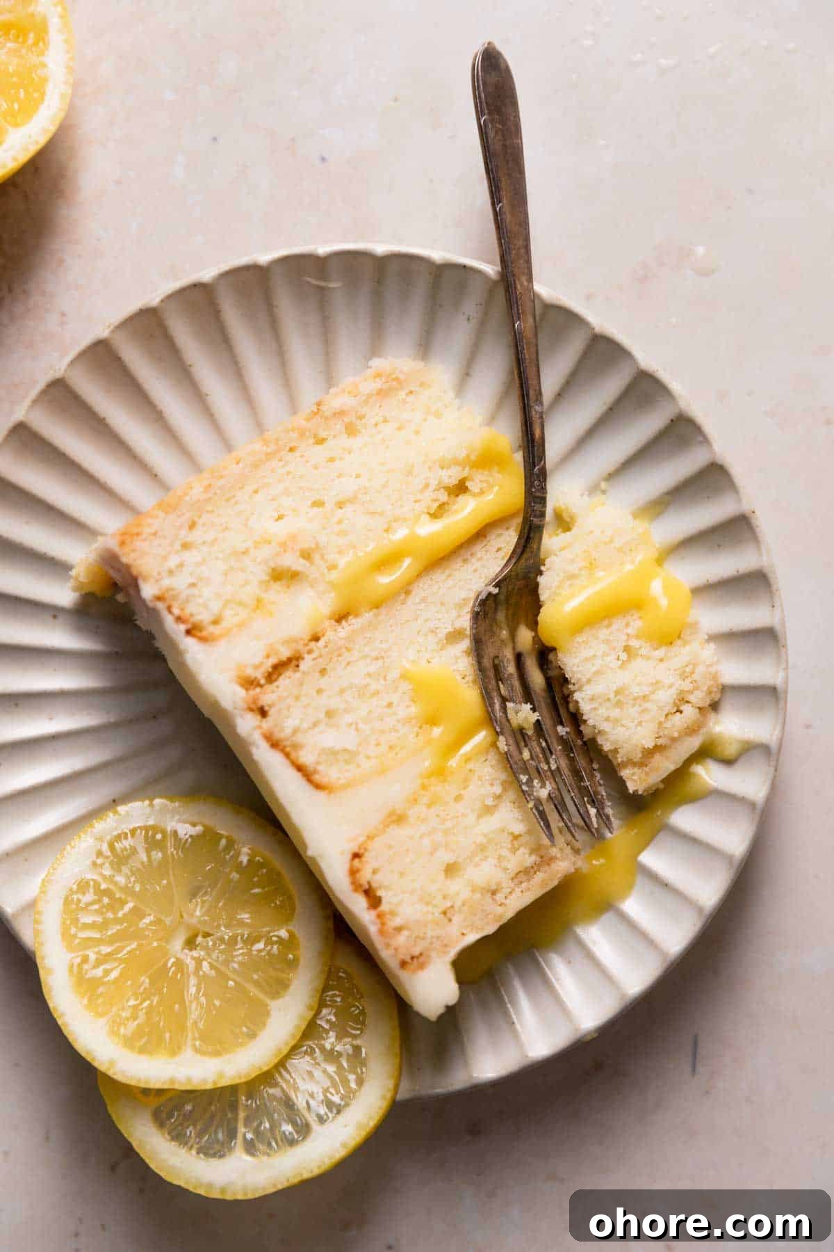Zesty Lemon Bar Cake Recipe with Tender Shortbread Crust 14 a slice of lemon bar cake on a white plate with fresh lemon slices.