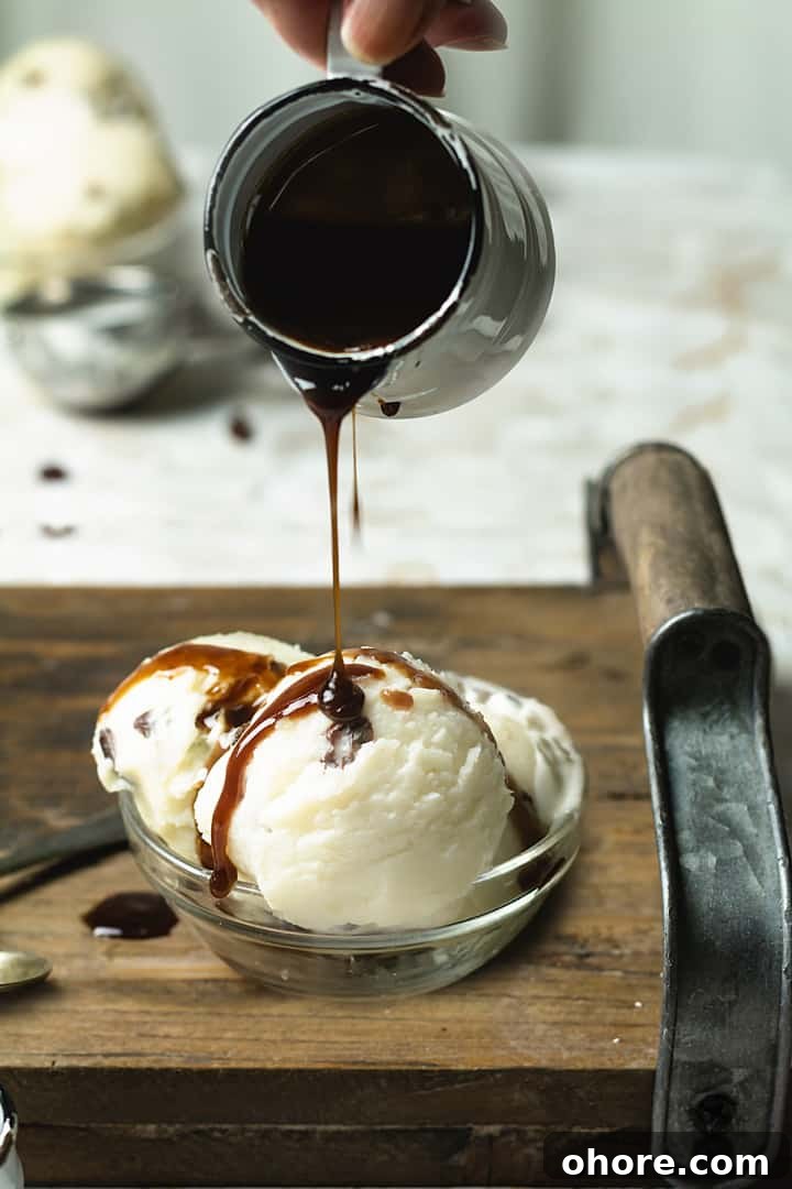 Rum and Raisin Gelato with Warm Rum Caramel Sauce 6 A bowl with three ice cream scoops on a wooden tray and rum sauce being poured over.
