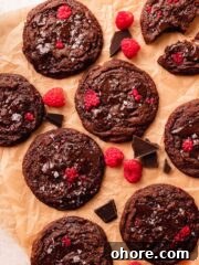 chocolate raspberry cookies on brown parchment paper with chocolate pieces and fresh raspberries around