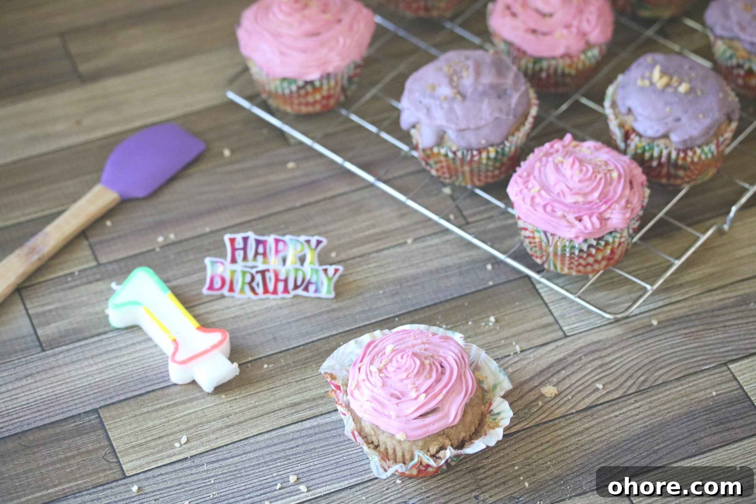 Pink and purple cupcakes with shimmer sprinkles on a cooling rack with a candle number one and happy birthday