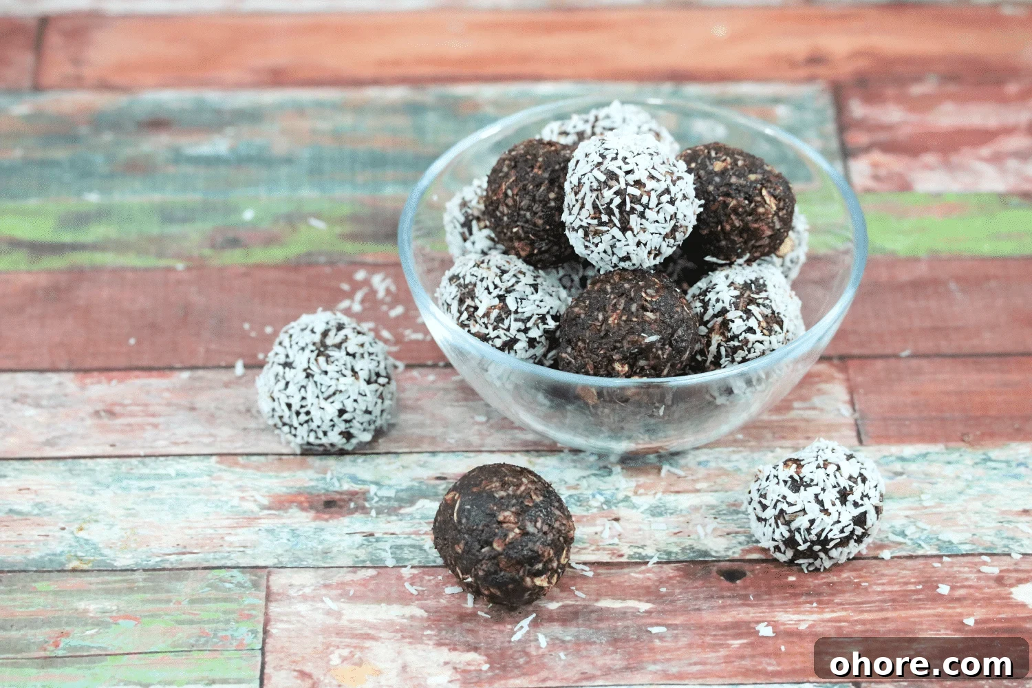 Chocolate coconut energy balls with dates in a glass bowl with three energy balls beside the bowl and coconut around it