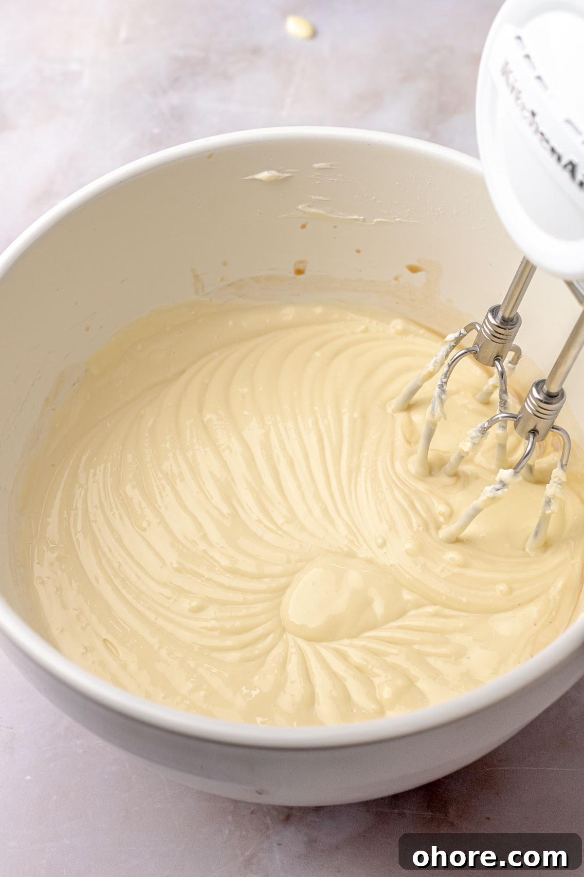 A hand mixes beats cheesecake filling in a bowl.