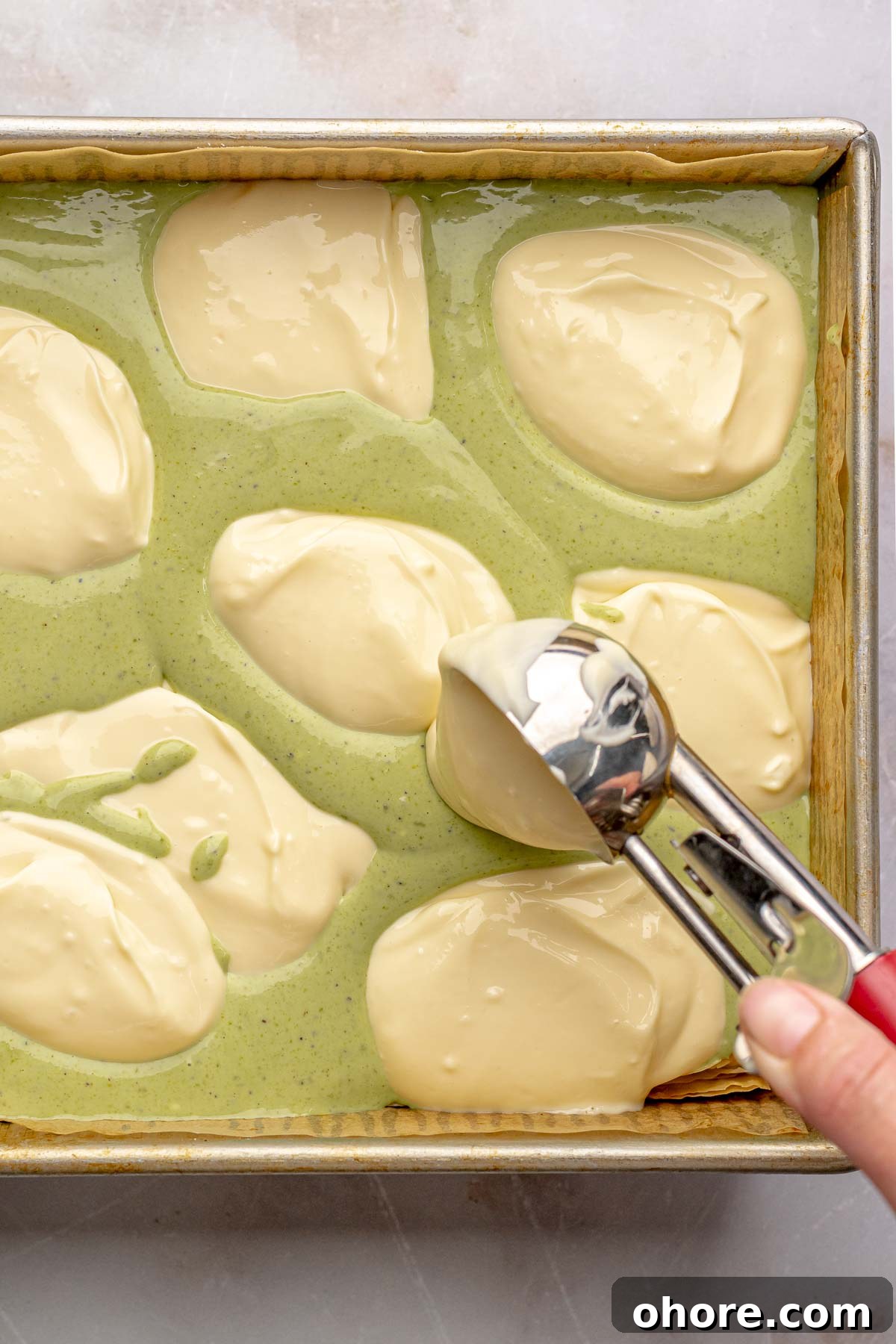 A cookie scoop adds a dollop of cheesecake batter into a pan.