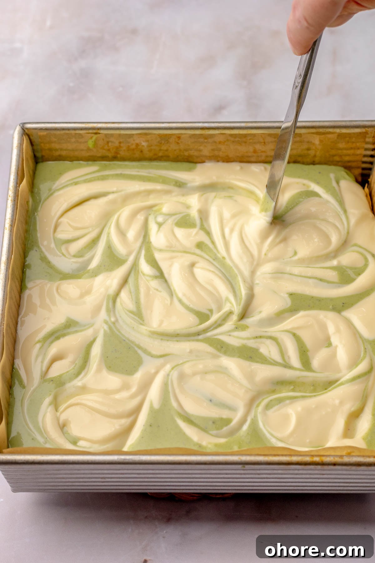 A butter knife swirls together cheesecake batters in a pan.