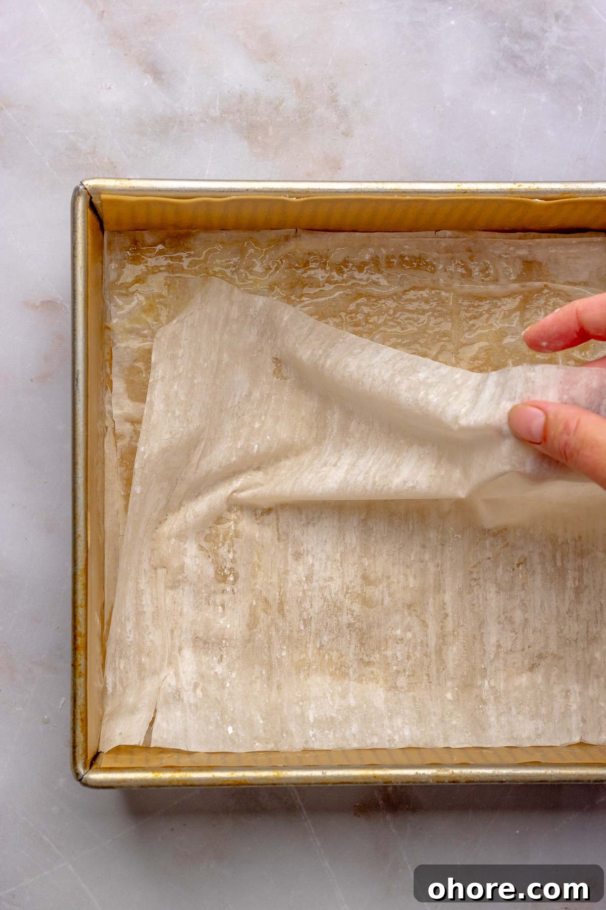 A hand adds a piece of phyllo pastry into a square pan.