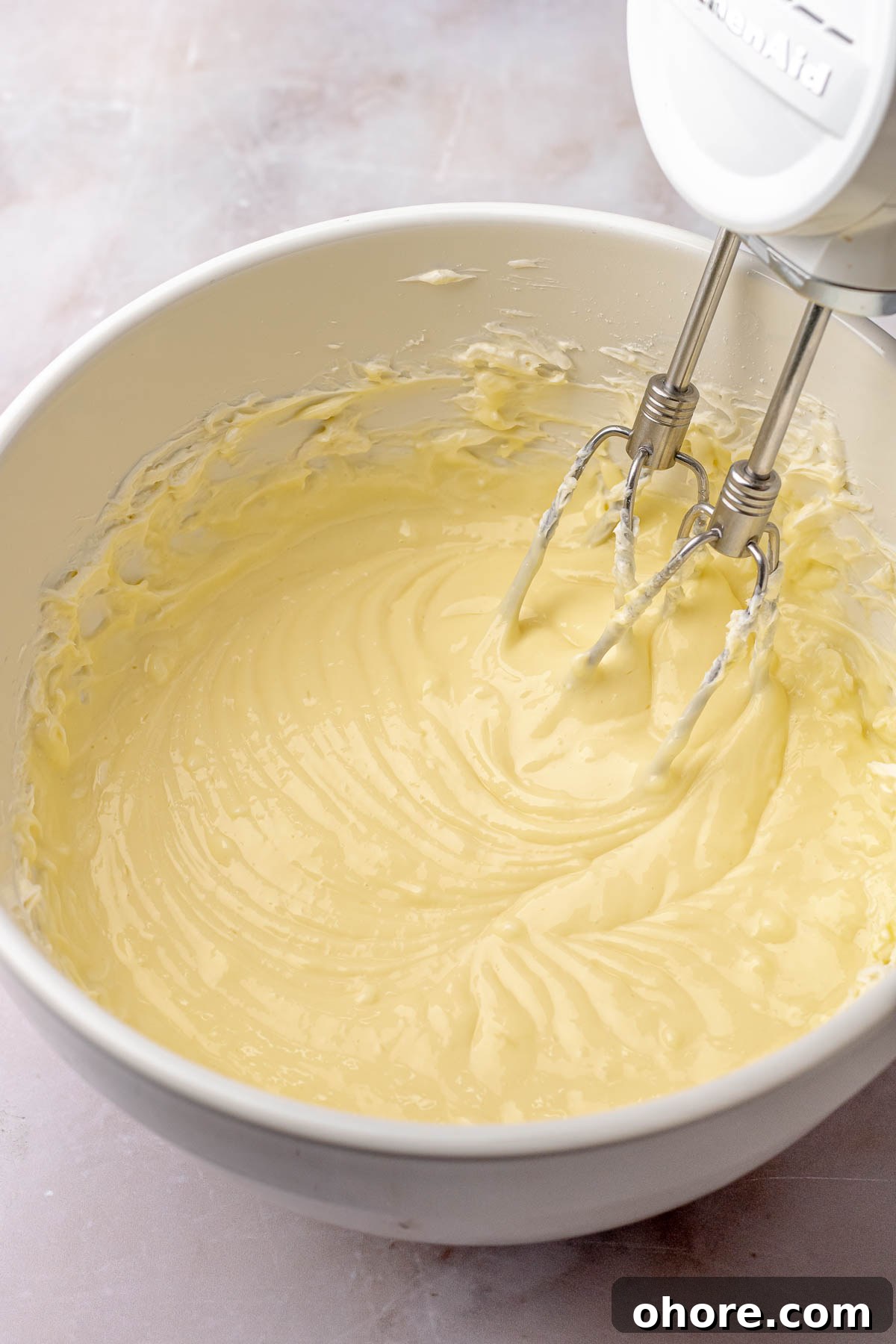 A hand mixes beats cheesecake filling in a bowl.