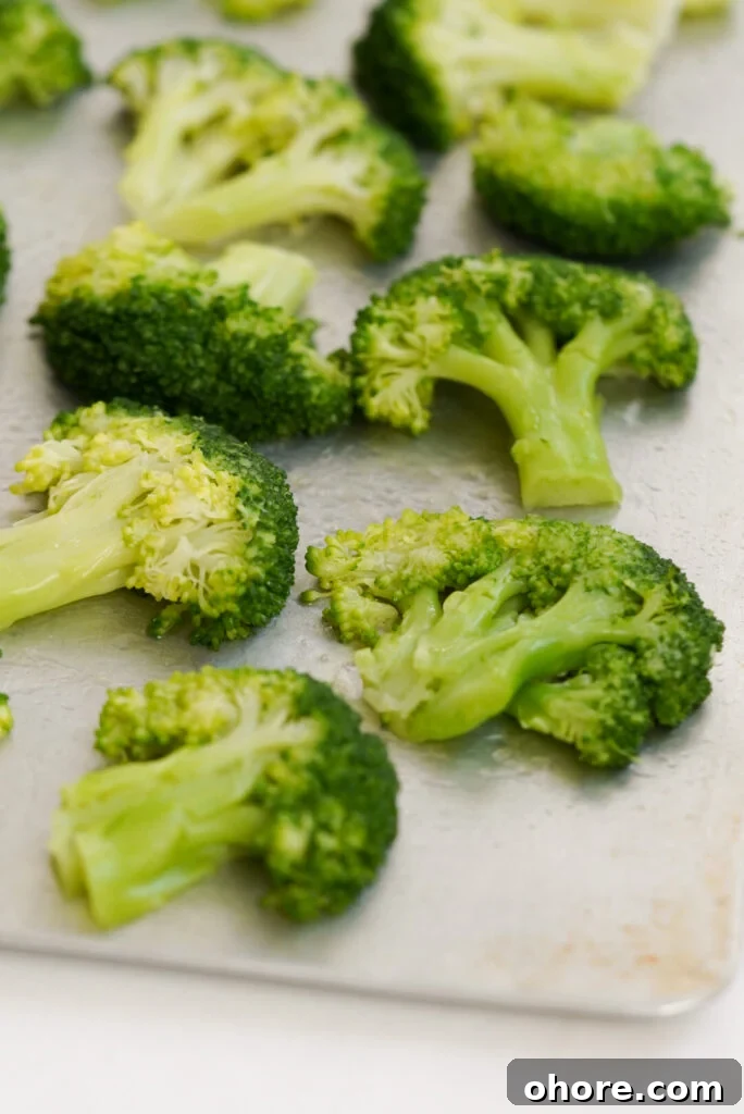 Crispy Smashed Broccoli with Parmesan and Garlic 7 closeup on broccoli florets on a baking sheet after being smashed with a cup.
