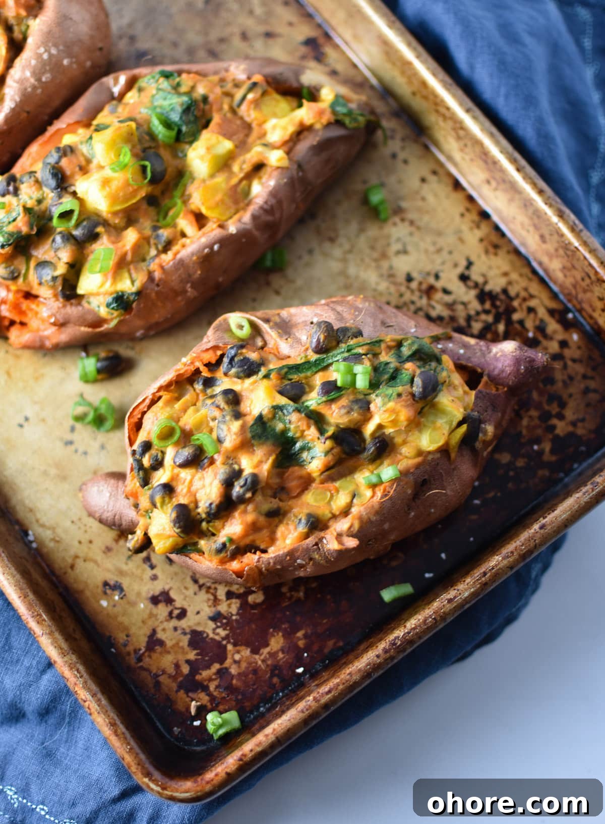 A stuffed sweet potato with Mexican-style filling topped with enchilada sauce on a baking sheet