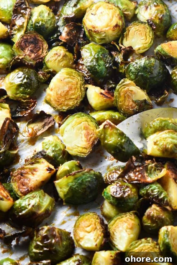 Roasted bang bang brussels sprouts on a baking sheet with a spoon flipping one