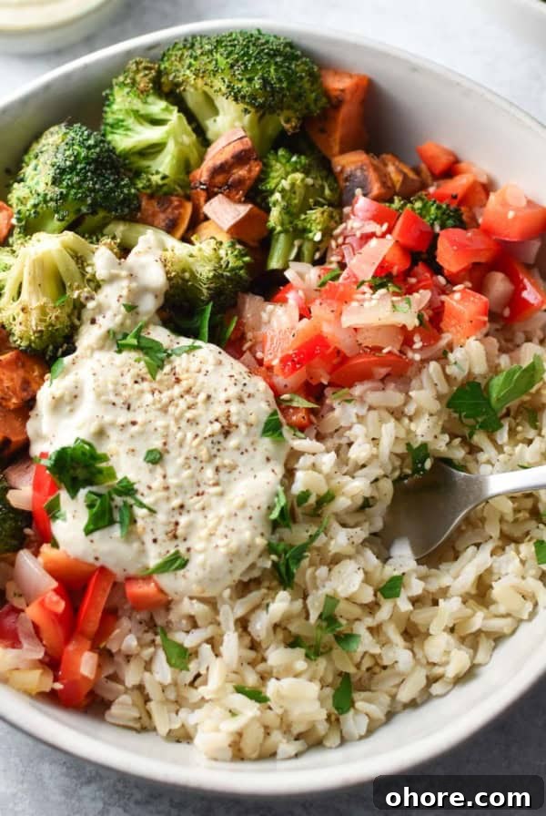Broccoli, sweet potatoes, and rice all topped with chopped veggies and a sauce with a fork placed on the side of the bowl.