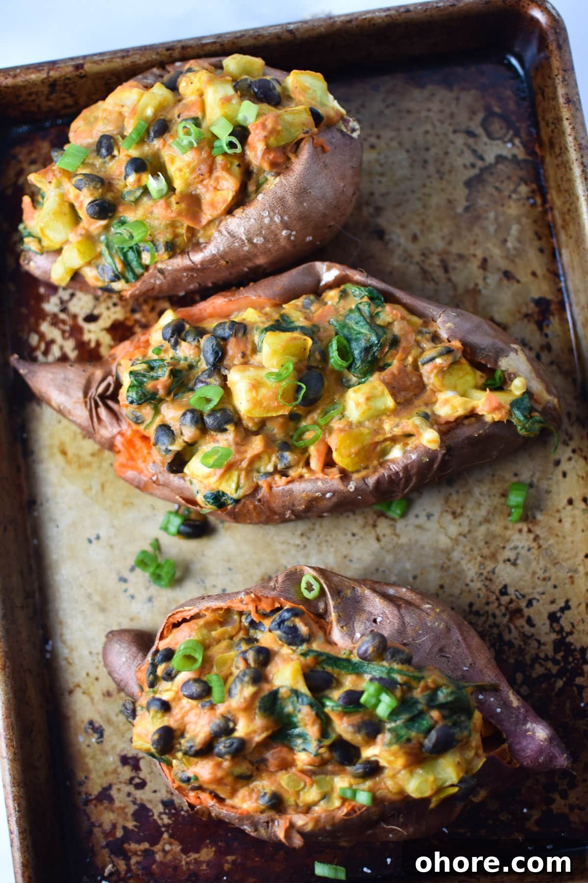 A sheet pan with three stuffed sweet potatoes topped with black beans, squash and green onion.