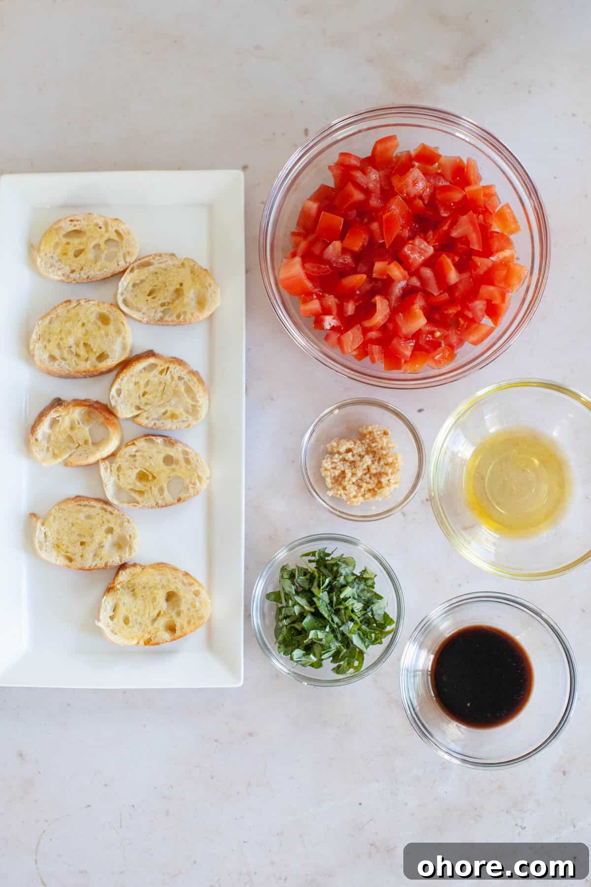Bruschetta ingredients separated into small glass bowls. Crostinis on a rectangular serving dish.