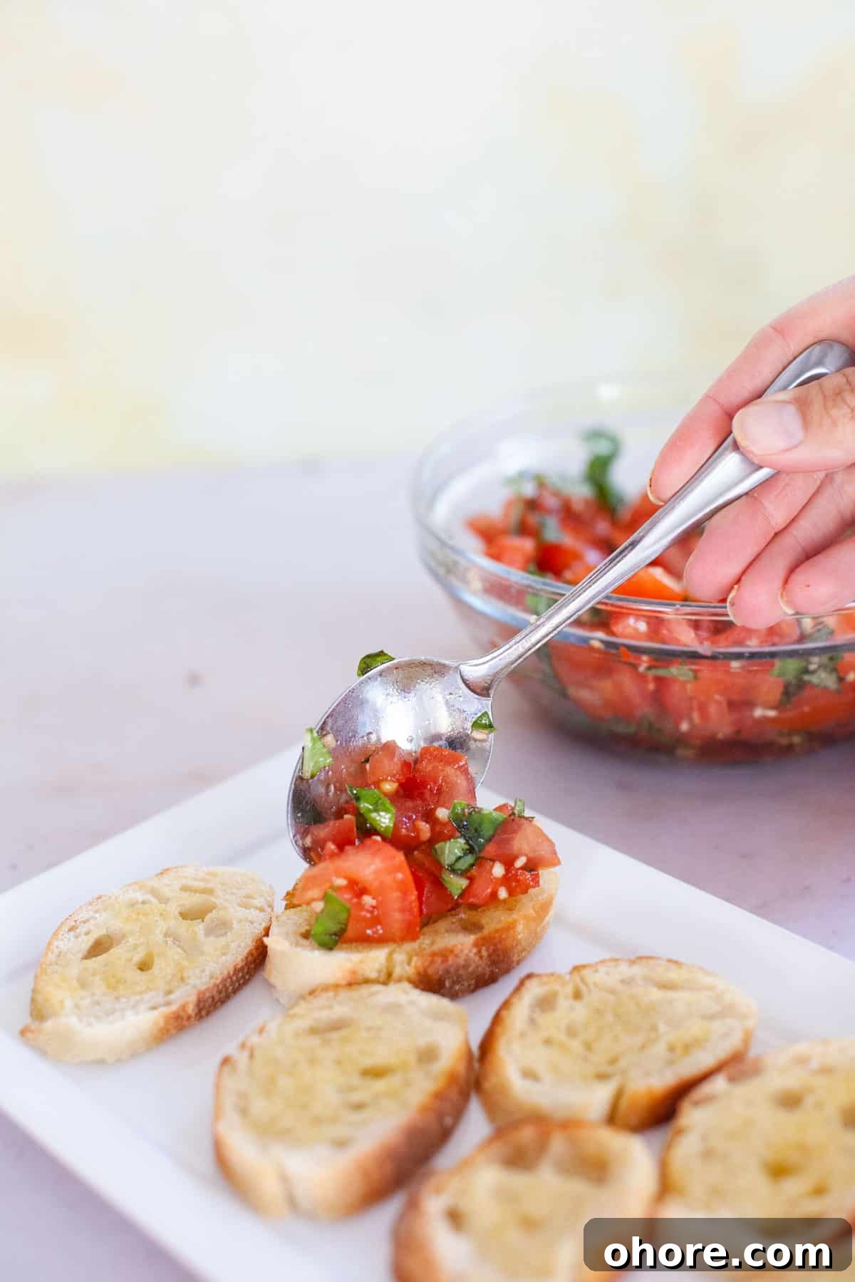 Bruschetta mix being placed on the crostini with a spoon.