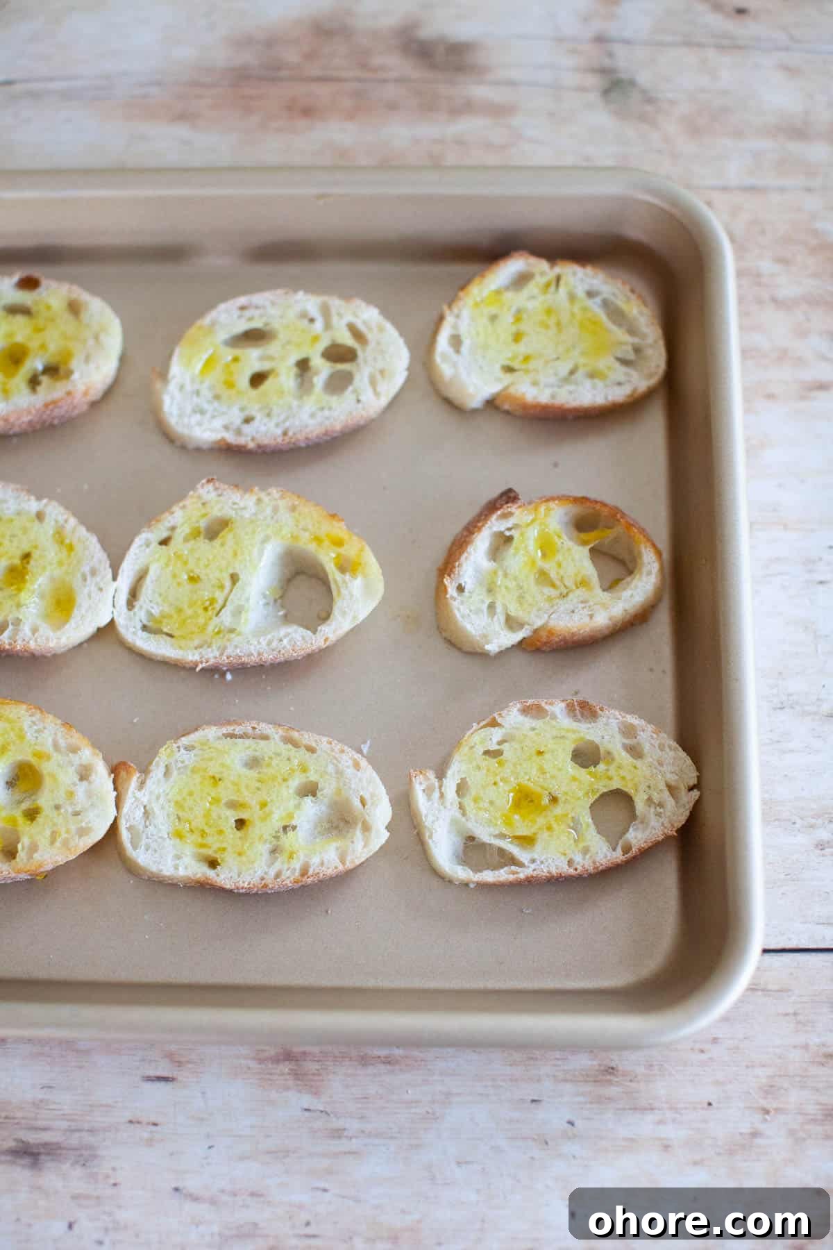 Slices of baguette, covered in olive oil, on a baking sheet