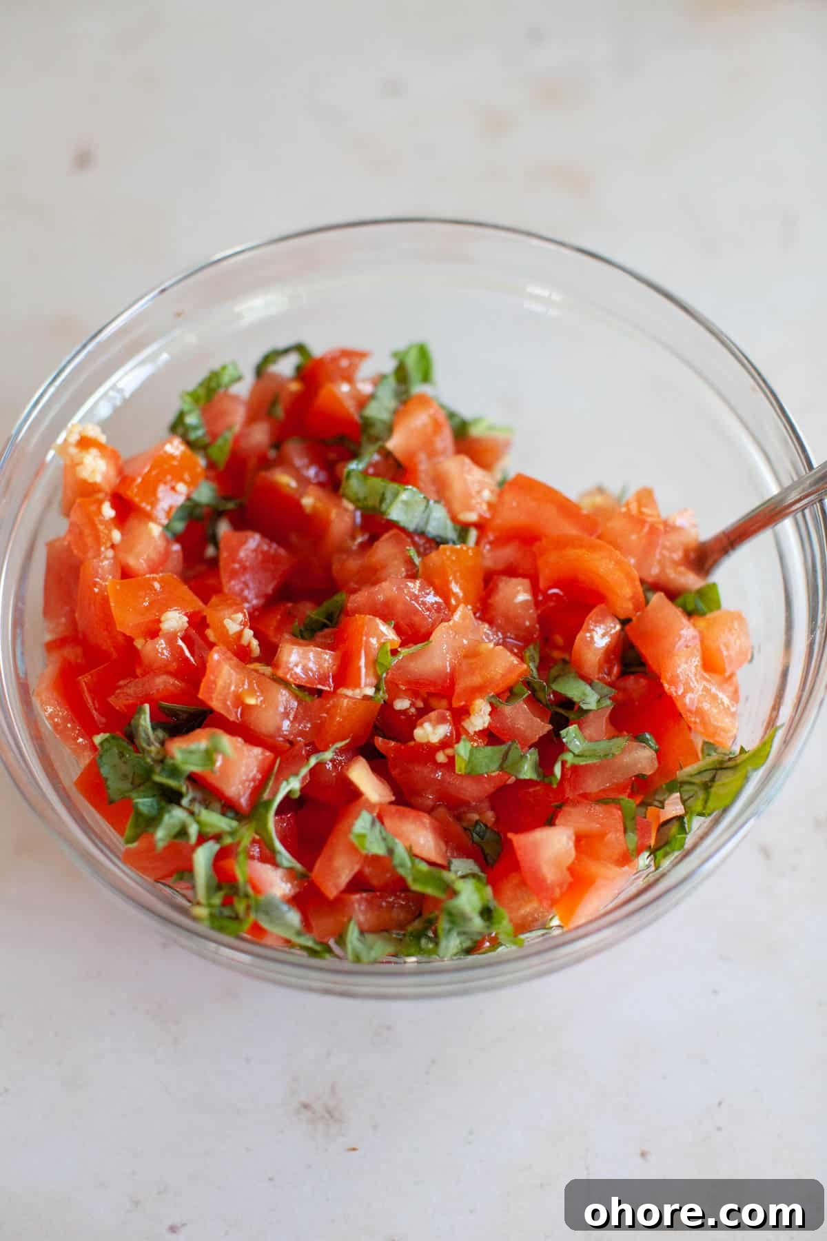 Bruschetta mix in a glass bowl with a small spoon.