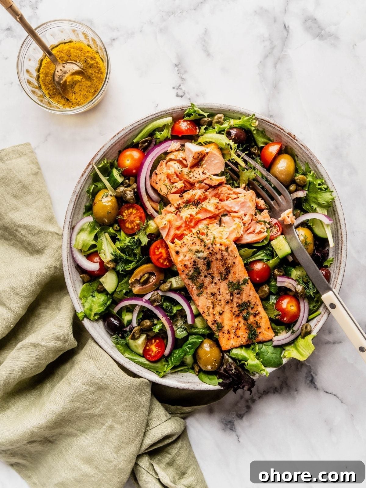 Mediterranean Salmon Salad bowl with flaky salmon over a bed of greens, tomatoes, olives and cucumbers.
